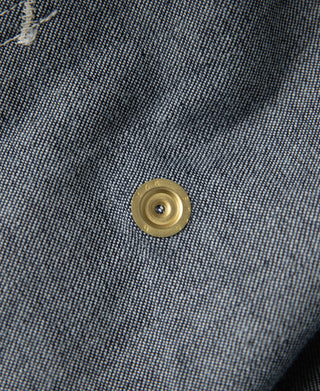 Indigo denim jacket button close-up with gold snap on dark wash fabric