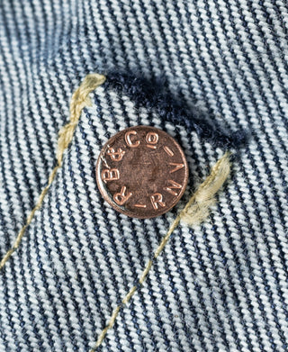 Copper rivet with lettering on indigo denim, with gold selvage thread