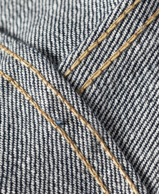 Indigo denim jacket pocket area with diagonal tan stitch detail