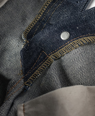Dark denim jeans waistband area with tan stitching and dark fabric button