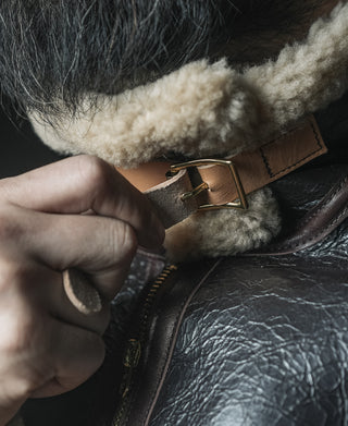 Dark brown leather jacket close-up: shearling cuff and brass buckle strap