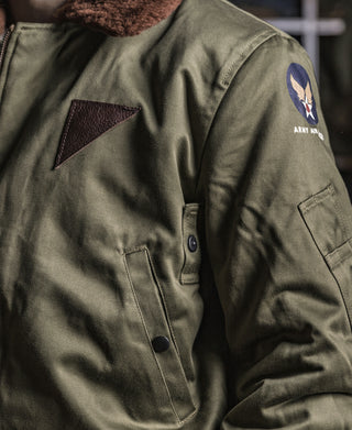 Olive flight jacket with brown leather trim, front zip, snap pockets, and sleeve patch
