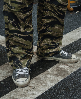 Tiger stripe camo fatigue pants with cargo pockets, shown with low-top sneakers