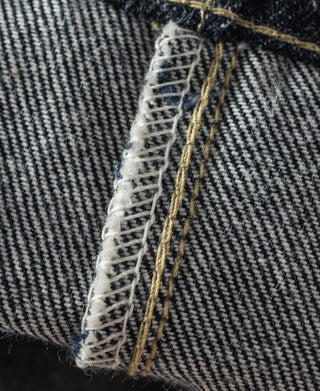 Indigo denim jeans inner hem with off-white stitching and gold-toned thread bar tacks