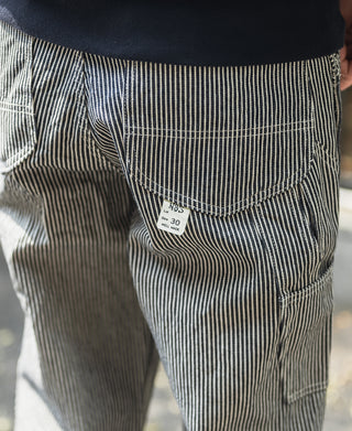 Striped carpenter pants pocket detail with stitched label and visible seam lines.
