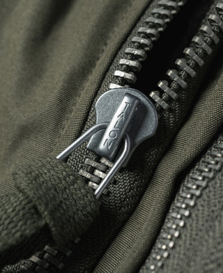 Olive flight jacket zipper with metal pull tab, close-up
