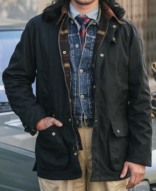 Black waxed chore jacket with snap buttons, field pockets, and hood with dark fur trim