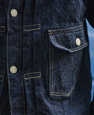Indigo denim jacket chest pocket detail with flap and metal snap buttons.