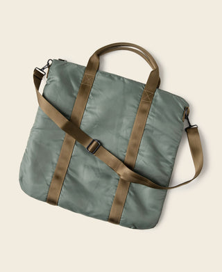 Sage green duffel-style helmet bag with crossbody strap, reinforced panels, brown webbing