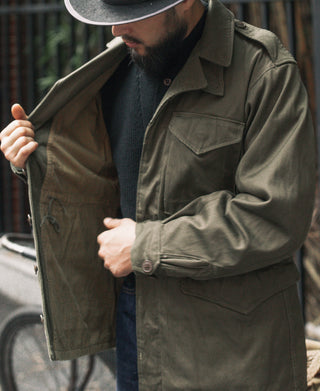 Olive field jacket worn by man, button front and flap chest pocket detail