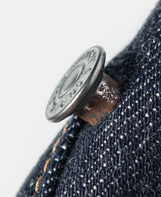 Metal jeans button with copper-toned rivet on indigo denim seam