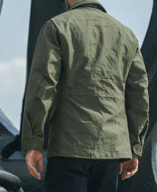Olive field jacket back with flap pocket and adjustable hem tabs.