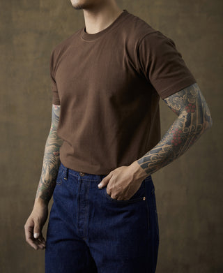 Coffee-brown crewneck cotton T-shirt on model, short sleeves with visible arm tattoos
