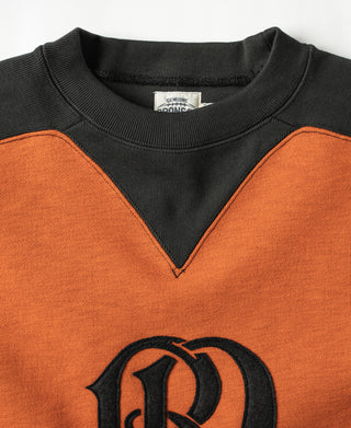 Orange sweatshirt with dark yoke V-inset and large black monogram logo at chest.
