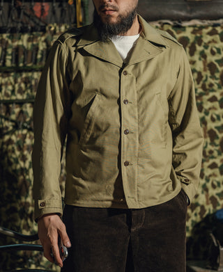 Olive green field jacket worn by man, button front and chest pockets visible