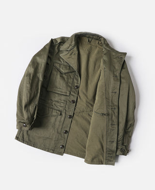 Olive M-1943 field jacket front laid flat with snap button placket and pockets