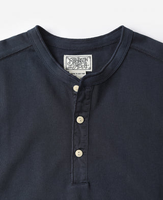 Navy henley shirt close-up with button placket, ribbed collar, and brand patch.