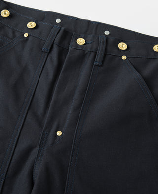Navy canvas pants detail: button fly front, belt loops, and brass hardware