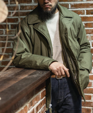 Olive flight jacket worn by man, front zipper and ribbed cuffs visible