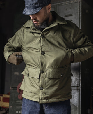 Olive flight jacket with button front and stand collar, model wearing cap