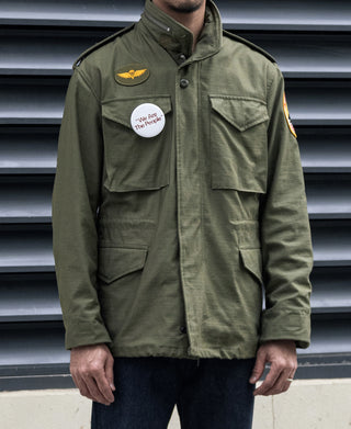 Olive M-65 field jacket front view with snap pockets and stand collar