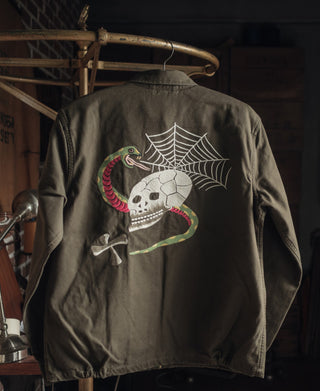 Dark gray-green souvenir jacket back with embroidered skull, web, and coiled snake