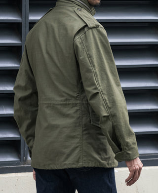 Olive M-65 field jacket worn over dark jeans, side view