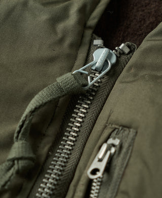 Olive flight jacket zipper track and metal pull tab close-up.