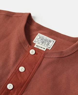 Brick red henley T-shirt neckline with three white buttons and brand label