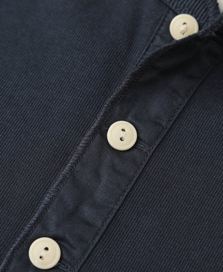 Navy henley shirt placket detail with three cream buttons and stitched edge.