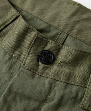 Olive fatigue trousers close-up of waistband button and stitched pocket flap.