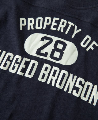 Navy t-shirt close-up: “PROPERTY OF 28” and “RUGGED BRONSON” printed across chest