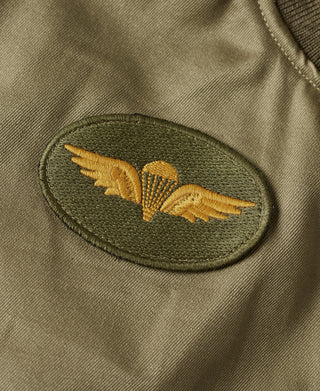 Olive jacket with embroidered wing patch on chest, stitched applique detail.