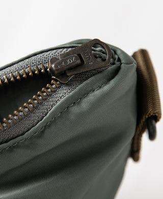 Close-up of sage green zipper with metal pull and brown leather-look tab
