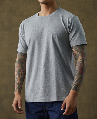 Gray cotton tubular T-shirt with crew neck, worn by a male model with tattooed arms.