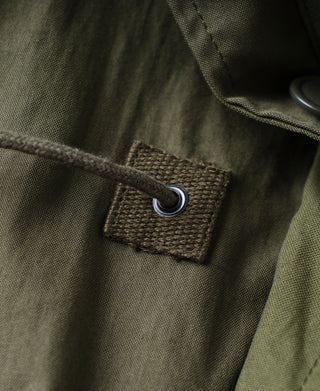 Olive parka chest pocket with fabric patch and metal grommet ring.