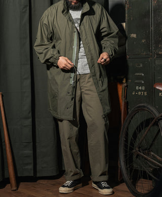 Olive field parka worn with hood open, front zipper, and adjustable waist.