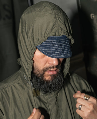 Olive parka with hood up and chin coverage, worn with denim-style cap.