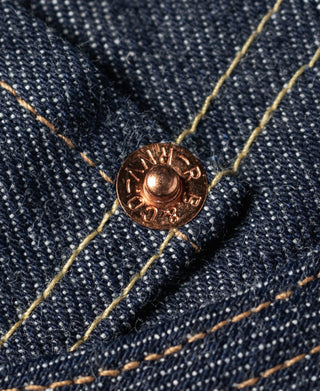 Copper-toned metal jeans rivet on dark blue denim with orange-brown contrast stitching