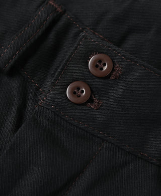 Close-up of black breeches with brown buttons and contrast stitching.