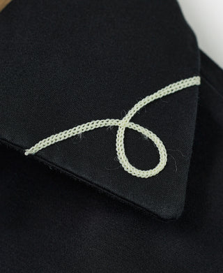 Black jacket shoulder close-up with embroidered loop letter details in light thread