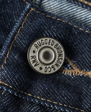 Copper-tone belt rivet on indigo denim with stamped logo text