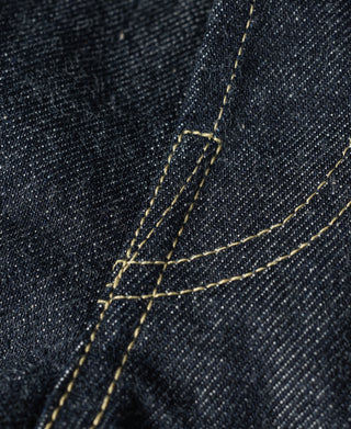 Indigo denim jeans close-up of curved seam and yellow topstitching detail.
