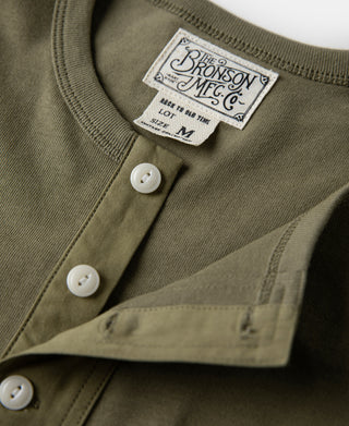 Olive henley t-shirt chest close-up with white buttons and Bronson Mfg woven label