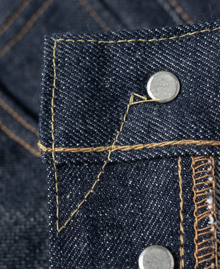 Dark denim jeans yoke corner with metal button rivet and golden topstitching.