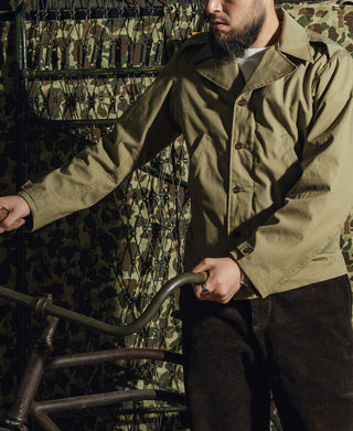 Olive green field jacket with button front, sleeve tabs, and chest pocket