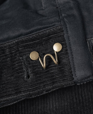 Black corduroy pants cuff with adjustable strap and metal rivet buttons.
