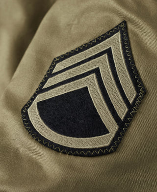 Embroidered shield patch on olive green tanker jacket sleeve with dark and light stripes