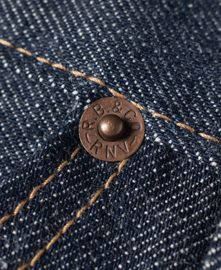 Dark denim jeans close-up of round coin rivet with brown metal finish.