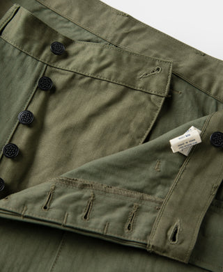 Olive fatigue trousers close-up of cargo pockets with button closures and fabric tag.